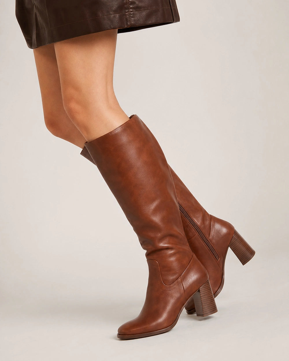 Cognac-brown knee-high boot showing the smooth finish, inner zip, rounded almond toe and sculpted stacked heel.