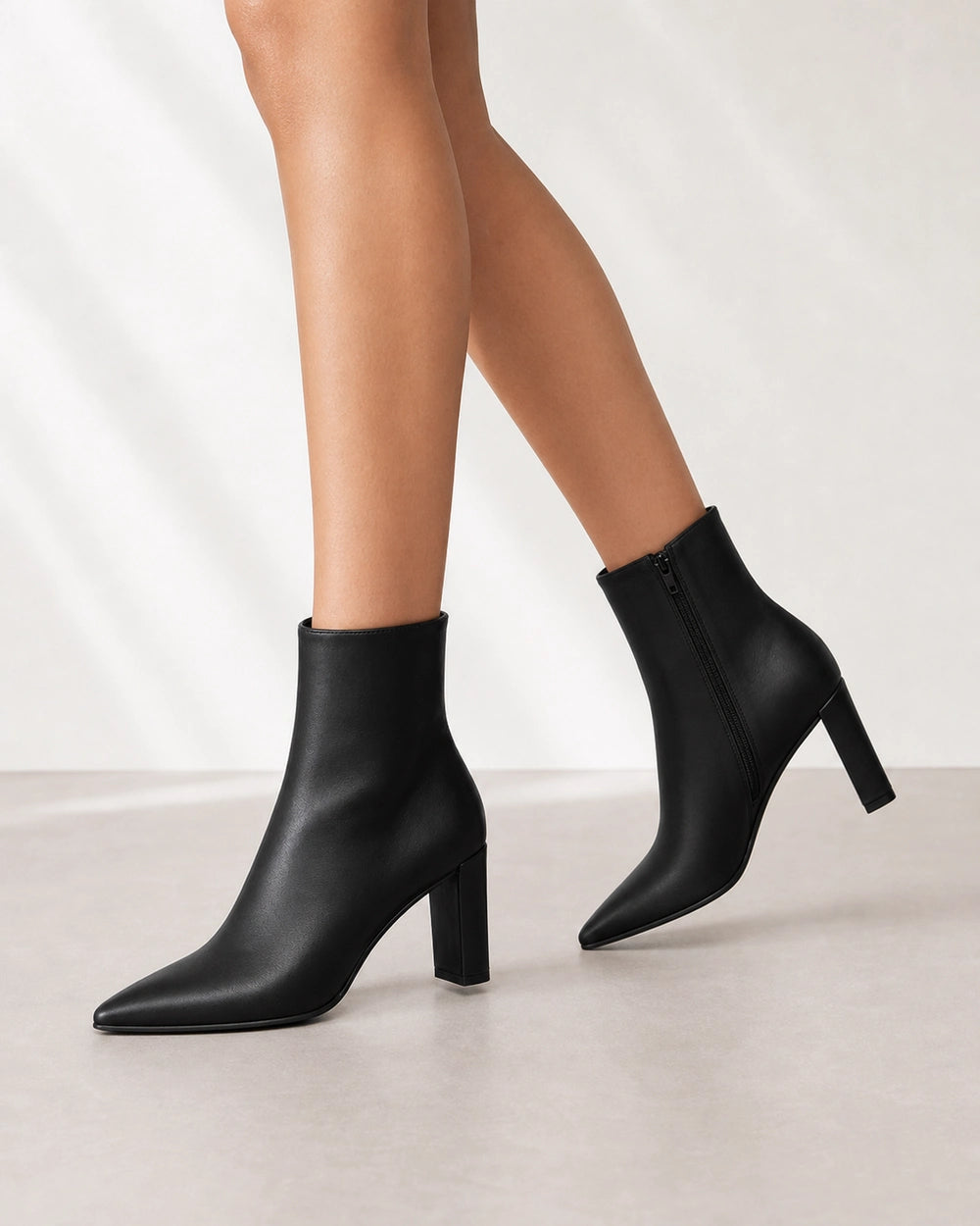 Women's black pointed-toe high-heel ankle boots, walking view.