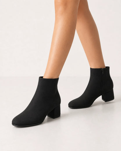 Women's minimalist black block-heel ankle boots, walking view.